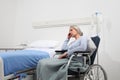 Sad and pensive elderly woman abandoned and forgotten isolated on wheelchair near bed in hospital room, concept of loneliness and Royalty Free Stock Photo
