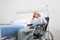 Sad and pensive elderly woman abandoned and forgotten isolated on wheelchair near bed in hospital room, concept of loneliness and Royalty Free Stock Photo