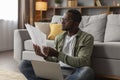 Sad pensive mature black man in glasses with laptop analyst document, work in living room interior Royalty Free Stock Photo