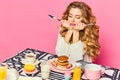 Upset beautiful girl with long hair holding cutlery and looking at pancaces with annoyed face over pink background Royalty Free Stock Photo