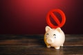 A sad piggy bank bears a prohibitory NO sign on its back. Confiscation of savings and bank deposits. Freeze and restrictions. Royalty Free Stock Photo