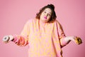 Sad plus size model with doughnuts, fat woman sadness and overeats on pink background