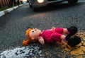 A sad plush toy doll is lying on the road near the wheel of a car. The concept of a road traffic accident