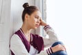 Sad pretty teenage girl sitting on windowsill