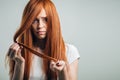 Sad redhead girl holding her damaged hair looking at camera. Royalty Free Stock Photo