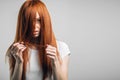 Sad redhead girl holding her damaged hair looking at camera. Royalty Free Stock Photo