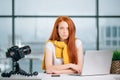 Sad redhead girl vlogger sitting at table with laptop and looking at camera. Royalty Free Stock Photo