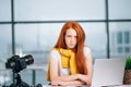 Sad redhead girl vlogger sitting at table with laptop and looking at camera. Royalty Free Stock Photo