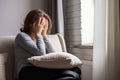 Sad scared woman covering her face with hands and crying. Lonely girl sitting near window with pillow on a sofa of apartments Royalty Free Stock Photo