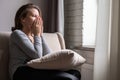 Sad scared woman covering her face with hands and crying. Lonely girl sitting near window with pillow on a sofa of apartments. Royalty Free Stock Photo