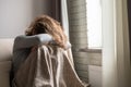 Sad scared woman in panic attack covering her face with hands and crying. Lonely girl wrapped in a plaid sitting near window Royalty Free Stock Photo