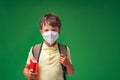 Sad schoolboy in a protective mask, standing on a green background