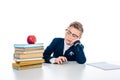 Sad schoolboy in glasses sitting at desk with books and apple isolated on white. Royalty Free Stock Photo