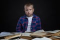 A sad schoolboy sits at a table with open books. Learning difficulties. Black background