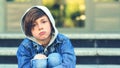 Sad schoolboy sitting on stairs outdoors. Unhappy boy in denim jacket with hood and a scraped knee. School bullying concept. Pre Royalty Free Stock Photo