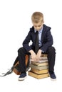 Sad schoolboy in a suit sitting on a pile of books, head bowed. Isolated on a white background.