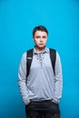 Sad schoolboy teenager with a school backpack behind his back on a blue background Royalty Free Stock Photo