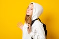 Sad teen girl with backpack. Cute girl dressed white hoodie on yellow background with backpack