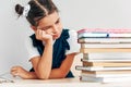 Sad schoolgirl looking on a pile of books on the desk against light grey background. Exhausted little girl learner has tired Royalty Free Stock Photo