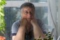 Sad senior woman behind window glass with raindrops. Female in deep thought looks through glass Royalty Free Stock Photo