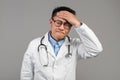 Sad sick funny adult asian man doctor in white coat, glasses touches forehead, suffers from fever