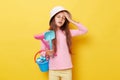 Sad sick unhappy little cute girl in panama holding beach sandbox toys rake and shovel isolated over yellow background suffering Royalty Free Stock Photo