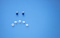 Sad smiley face made of blue and white tablets and pills on blue background top view with copy space for text. Royalty Free Stock Photo