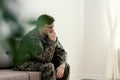 Sad soldier in uniform covering his mouth while sitting on a sofa Royalty Free Stock Photo