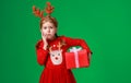 Sad, surprised funny child girl in red Christmas reindeer costume with gift on green   background Royalty Free Stock Photo