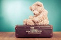 Sad Teddy Bear toy sitting on old retro suitcase front mint blue background. Vintage style photo Royalty Free Stock Photo