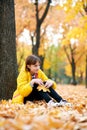 Sad teen girl sits near tree in autumn park. Bright yellow leaves and trees Royalty Free Stock Photo