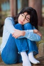 Sad teen girl sitting on rocks along lake shore, lonely expression