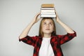 Sad teenage girl holding many books on her head, educational difficulties. A heavy burden of training