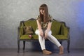 Sad teenage girl sits on green sofa. On gray background. Studio. Royalty Free Stock Photo