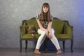 Sad teenage girl sits on green sofa. On gray background. Studio. Royalty Free Stock Photo