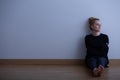 Sad teenage girl suffering from loneliness, sitting alone on the floor, copy space on empty wall