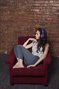 Sad teenager girl listening to music on headphones cringing herself in an old chair in an abandoned factory building Royalty Free Stock Photo