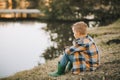 Sad thinking dreaming kid boy sits near a river or lake