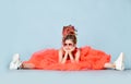 Sad thoughtful girl with colorful dreadlocks in coral big dress, sneakers, sunglasses sits on floor legs wide apart Royalty Free Stock Photo