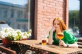 Sad depressed young woman drinking cocktail through straw sitting at table in outdoor cafe in sunny summer day. Royalty Free Stock Photo