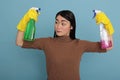 Sad tired asian housewife raising arms holding two detergent sprays Royalty Free Stock Photo