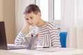 Sad tired boy sitting at table with books and laptop computer at home. Learning difficulties, online education concept Royalty Free Stock Photo