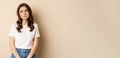 Sad and tired brunette woman looking drained and unamused, standing with pokerface against beige background