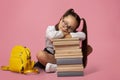 Sad and tired concept. Girl in glasses in uniform with backpack sleeps on stack of books Royalty Free Stock Photo