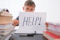 Sad tired frustrated boy sitting at the table with many books and holding paper with word Help. Learning difficulties Royalty Free Stock Photo