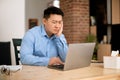 Sad tired middle aged asian man working on laptop computer, sitting at workplace at home office, free space Royalty Free Stock Photo