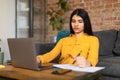 Sad tired spanish lady student making notes, sitting at table with laptop, studying in room interior at home Royalty Free Stock Photo