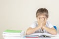 Sad tired upset schoolboy covering face with his hands sitting near table with pile of school books and notebooks Royalty Free Stock Photo