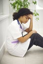 Sad tired young african american nurse sitting on floor in clinic, feeling overwhelmed by workload Royalty Free Stock Photo