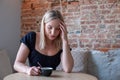 Sad tired young woman with a coffee in a cafe touching forehead having headache migraine or depression, upset frustrated Royalty Free Stock Photo